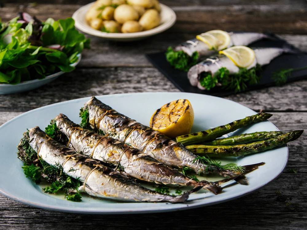 Hel grillet makrell på en tallerken med asparges og sitronbåter, omgitt av grønnsaker og tilbehør på bordet.
