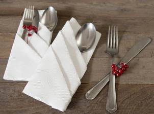To sett med bestikk med hvite servietter brettet pent, dekorert med små røde bær, ligger på et trebord.
