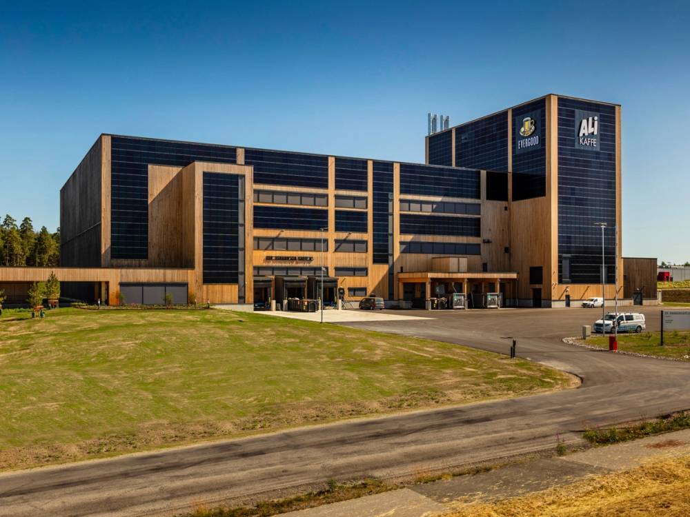 Et stort kontorbygg med flere etasjer, omgitt av en gresslette og en vei, under en klar blå himmel.