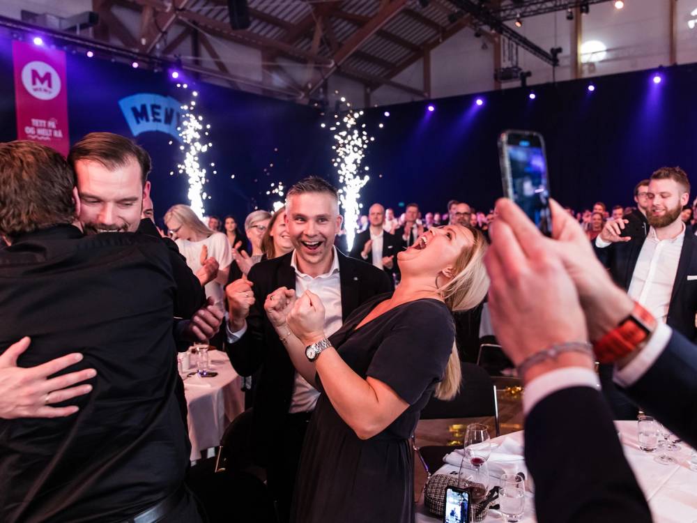 En gruppe mennesker feirer med konfettirør på en fest eller et arrangement, med mange som tar bilder og ser glade ut.