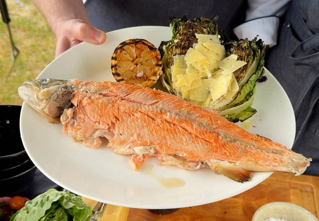 En person holder en stor tallerken med en hel steinbitt, kokt halibut, og en halvt oppskåret sitron, med grønnsaker og poteter ved siden av, i Kristiansand.