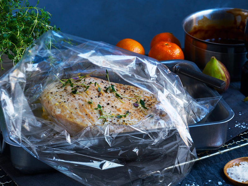 Kalkunfilet i stekepose med urter, klar til å bli stekt, omgitt av grønnsaker og krydder på en kjøkkenbenk.