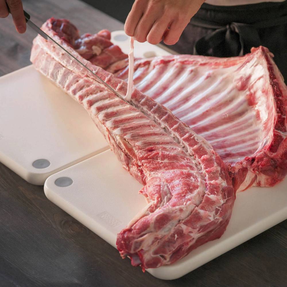 Person skjærer opp en stor ribbe av pinnekjøtt på et skjærebrett.