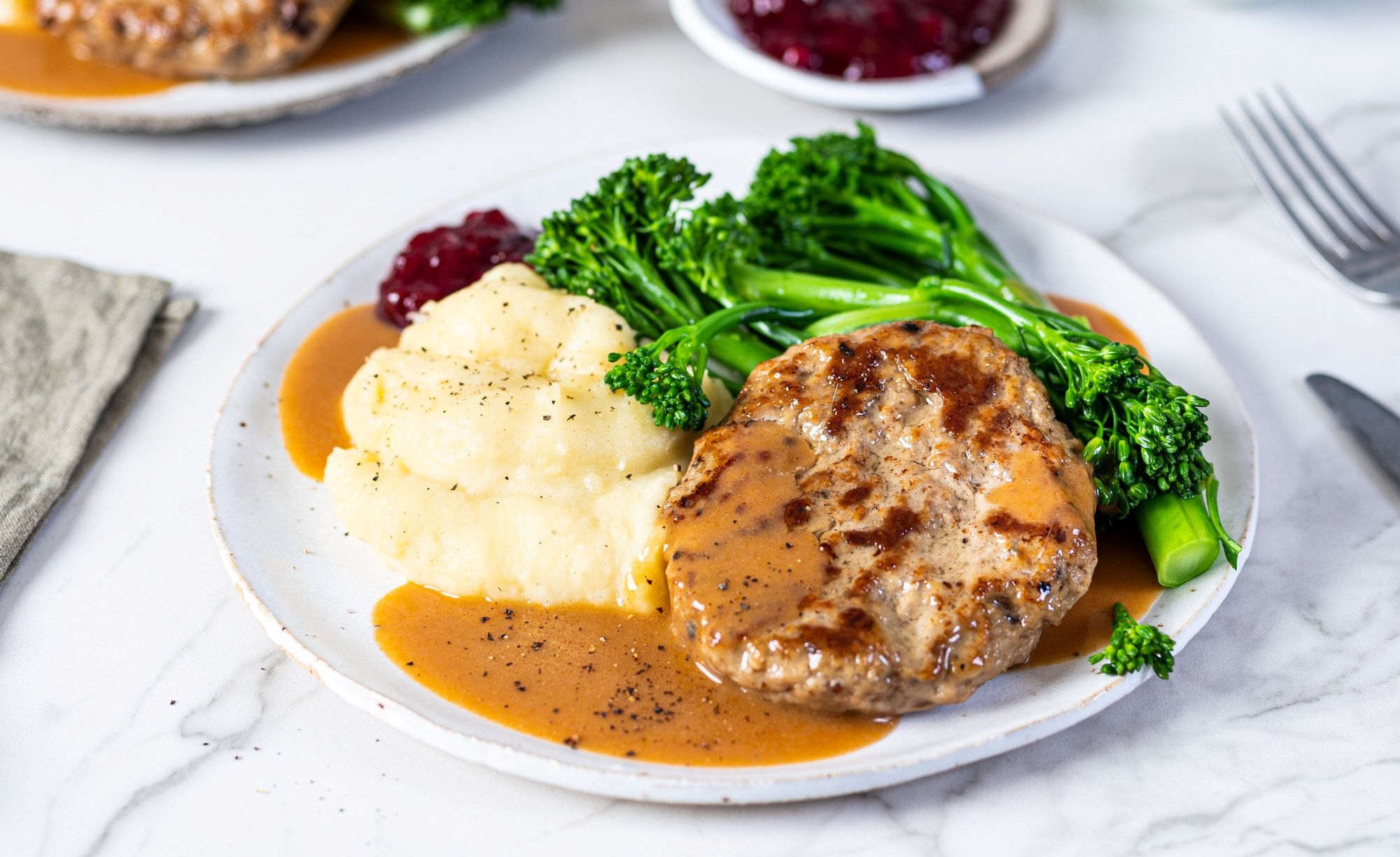 Stekt kjøttkaker med brun saus, potetmos og grønnsaker som brokkoli på en tallerken.