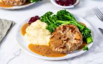 Stekt kjøttkaker med brun saus, potetmos og grønnsaker som brokkoli på en tallerken.