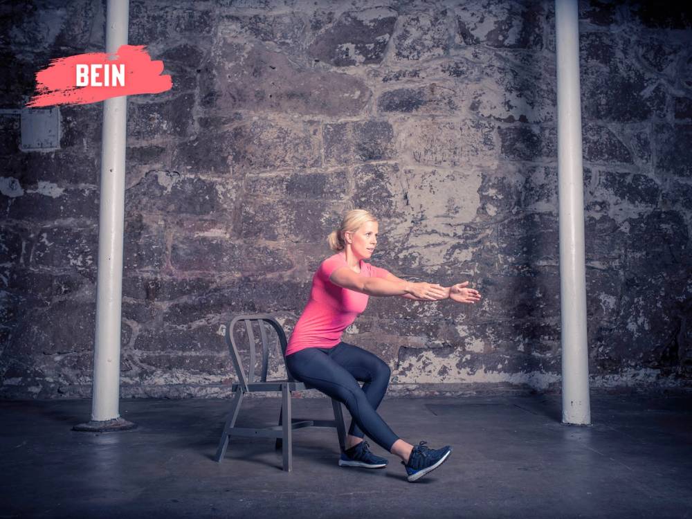 En person som utfører en knebøy mens de sitter på en stol foran en murvegg, med en merket pil som peker på beinet.