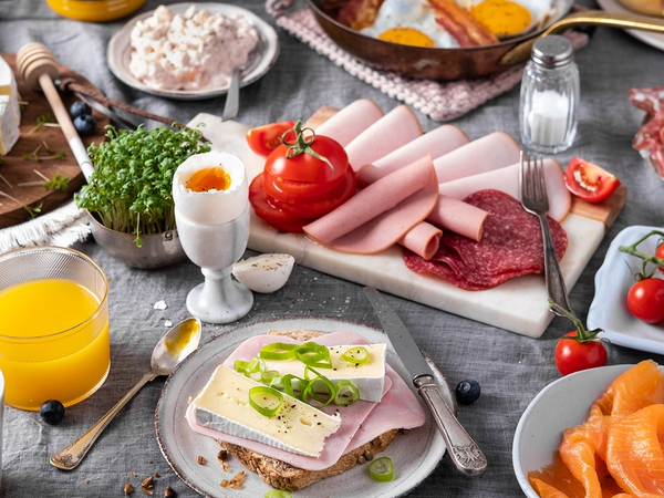 Et frokostbord med pålegg, egg, tomater, juice og bakverk, klar for helgehelg.