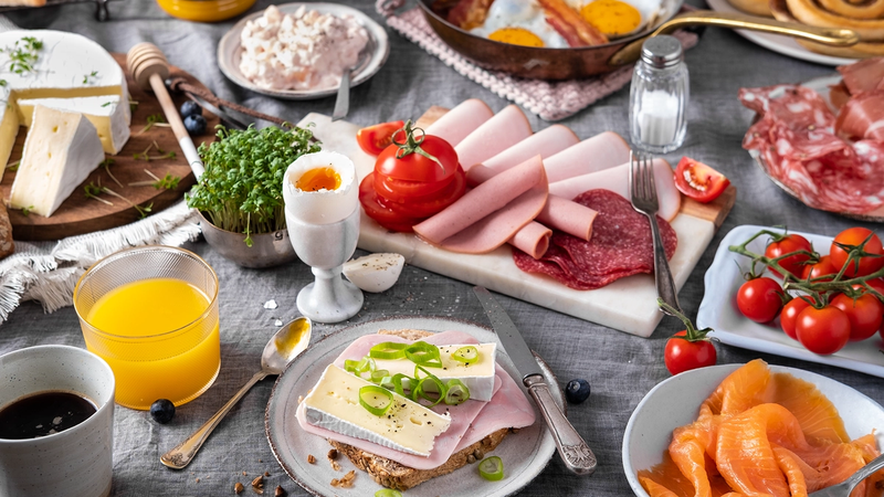 Et frokostbord med pålegg, egg, tomater, juice og bakverk, klar for helgehelg.