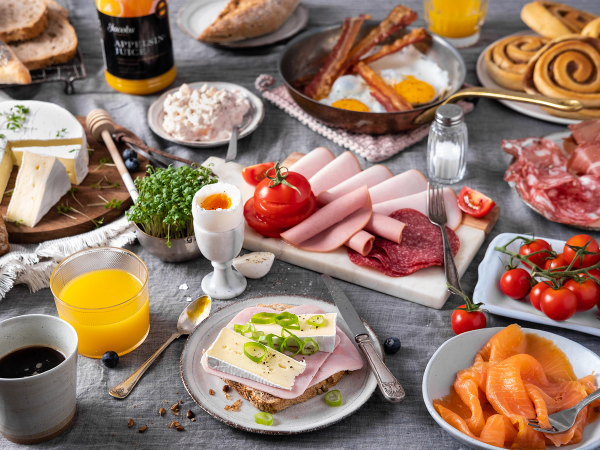 Et frokostbord med pålegg, egg, tomater, juice og bakverk, klar for helgehelg.