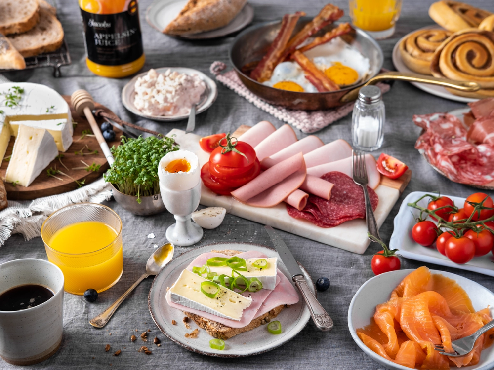 Et frokostbord med pålegg, egg, tomater, juice og bakverk, klar for helgehelg.
