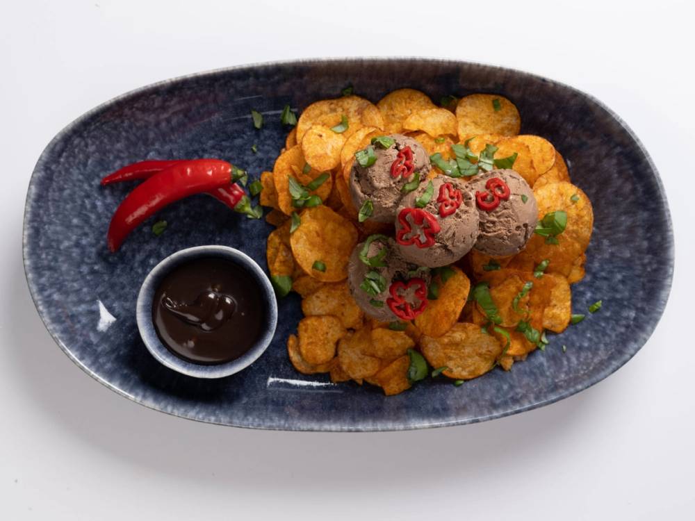 En tallerken med iskrem toppet med små kaker og pyntet med små grønne blader, sammen med en liten skål med sjokoladesaus og to røde chili på siden.