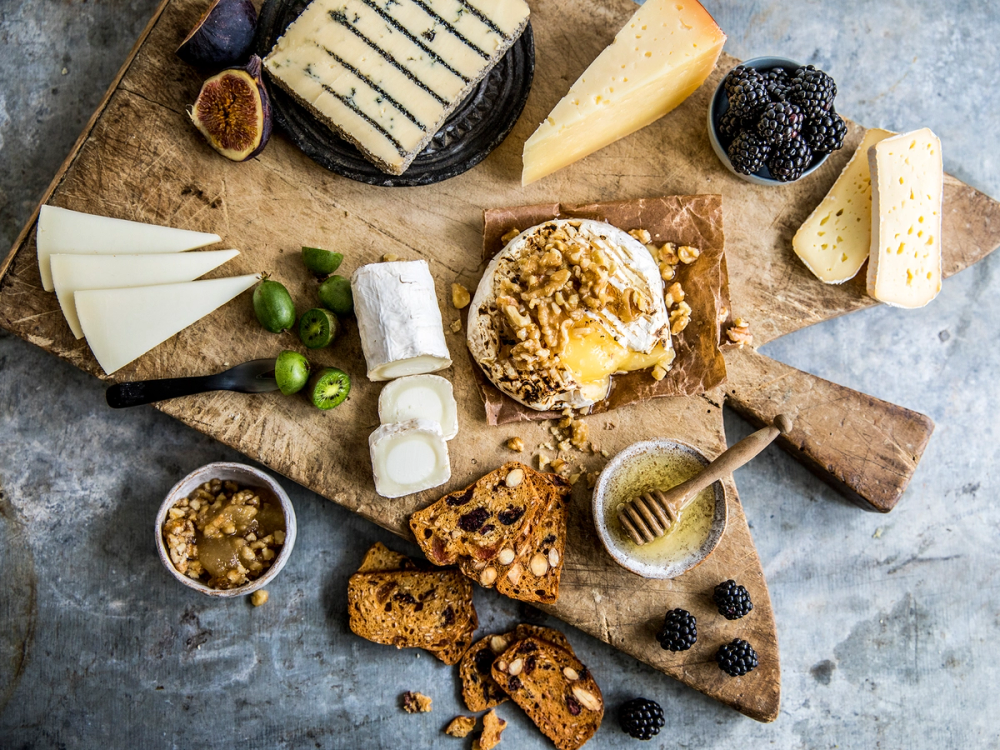 Et ostefat med ulike typer ost, kjeks, druer og honning, servert på et trebrett.