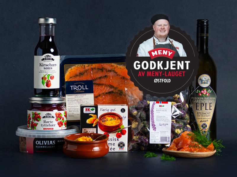 Et utvalg av matvarer og drikke, inkludert syltetøy, krydder, fisk og en flaske alkohol, på et bord, med en person som holder et skilt med teksten 'Godkjent av Meny-Lauget Østfold'.