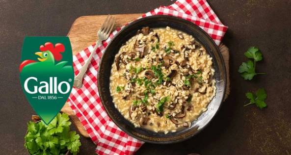 Risotto med sopp og urter i en svart panne på et bord med en rød og hvit sjekkeklut og noen friske urter ved siden av.