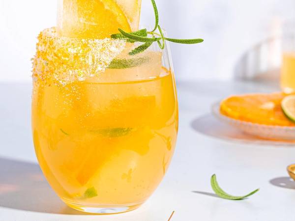 Mocktail med sitrusfrukter og mynte i et glass, pyntet med sitronskive og sukkerkant, på et lyst bord.