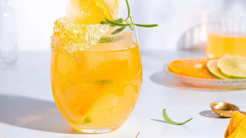 Mocktail med sitrusfrukter og mynte i et glass, pyntet med sitronskive og sukkerkant, på et lyst bord.
