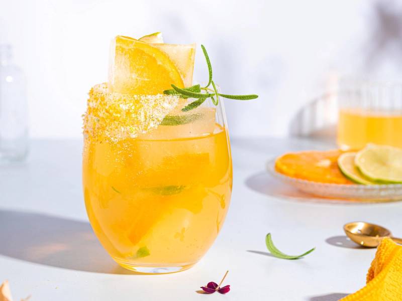 Mocktail med sitrusfrukter og mynte i et glass, pyntet med sitronskive og sukkerkant, på et lyst bord.