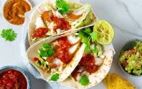 To torsketacos med salat, salsa og sitron på en tallerken, omgitt av små skåler med salsa og guacamole.