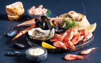 Et utvalg av skalldyr som reker, blåskjell og østers på en steinplate med sitronbåter og dipp, klar for helgekos.