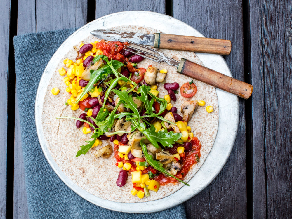 Vegetartaco med mais, tomat, rucola og kikerter på en tallerken med bestikk ved siden av