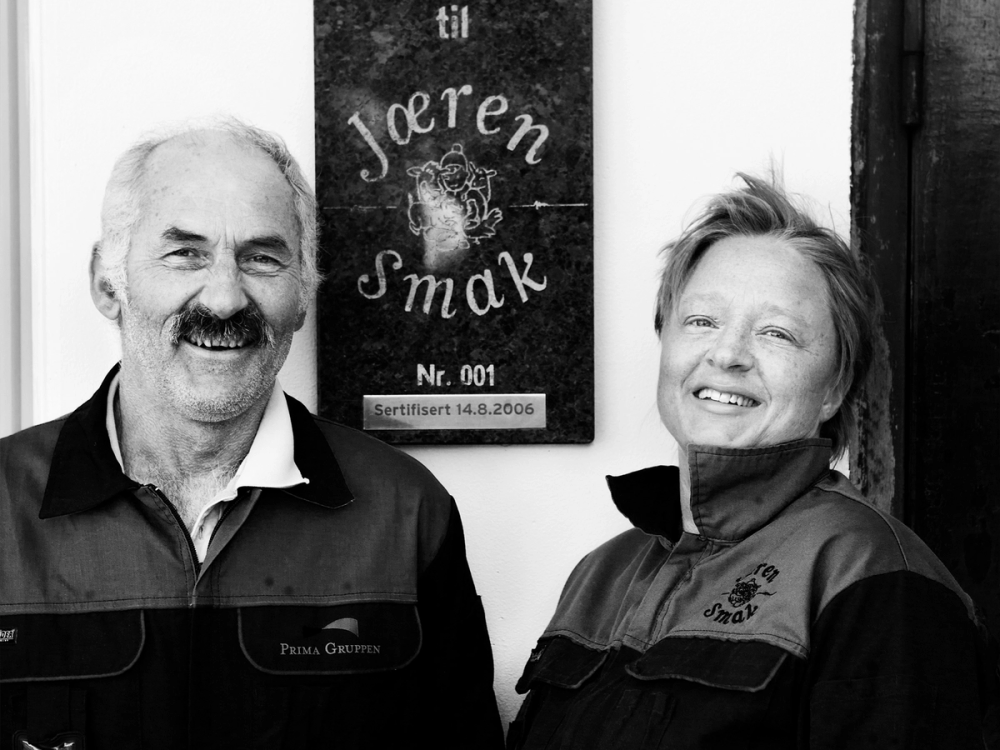 To personer står foran en tavle med teksten 'Joeren Smak' og en logo, og de ser ut til å delta i en smaking eller arrangement på Jæren.