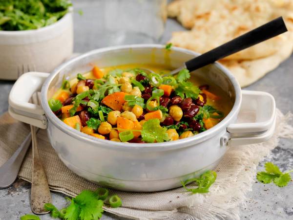 En vegetarisk gryte med kokosmelk, gulrøtter, kikerter og grønnsaker i en hvit gryte på et bord.