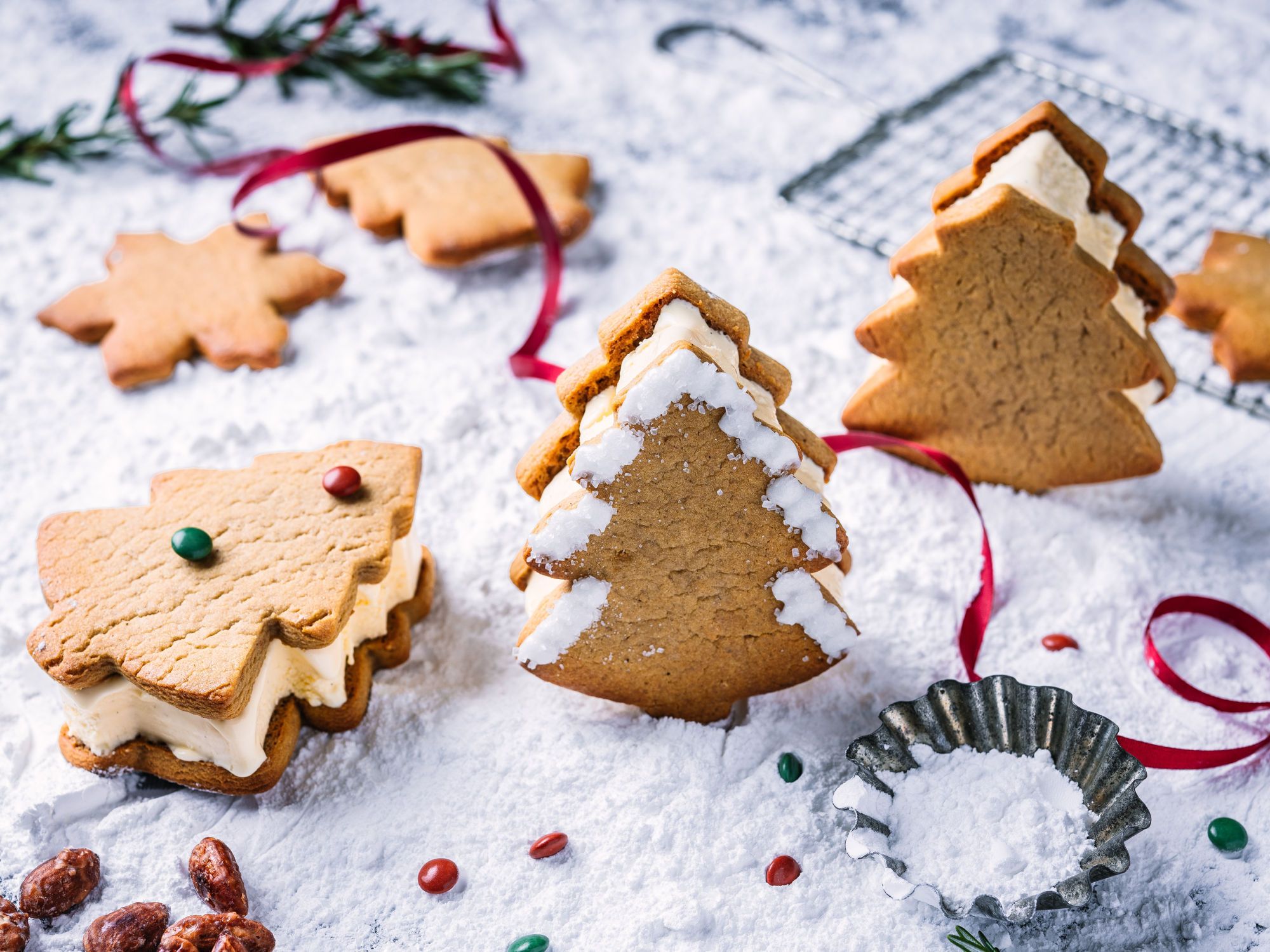 Pepperkaker i ulike former og med ulike dekorasjoner, plassert på et bord med julepynt og bakeutstyr.