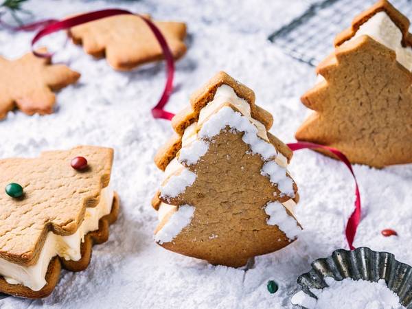 Pepperkaker i ulike former og med ulike dekorasjoner, plassert på et bord med julepynt og bakeutstyr.