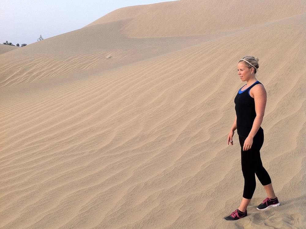 En kvinne går opp en sanddyne i ørkenen med en klar blå himmel i bakgrunnen.