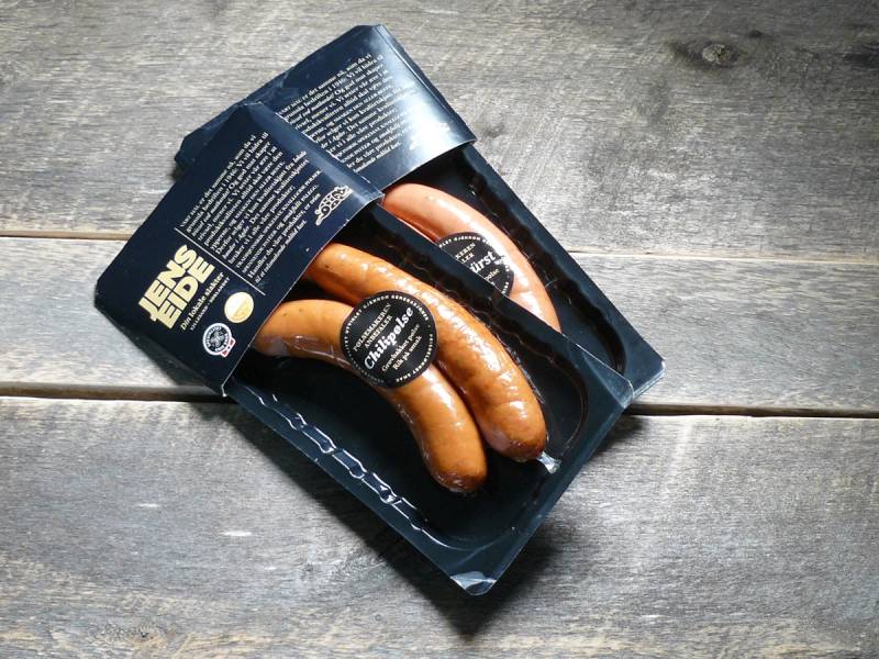 Pakke med tre grillpølser på en treoverflate, med emballasjen åpen og pølsene synlige.