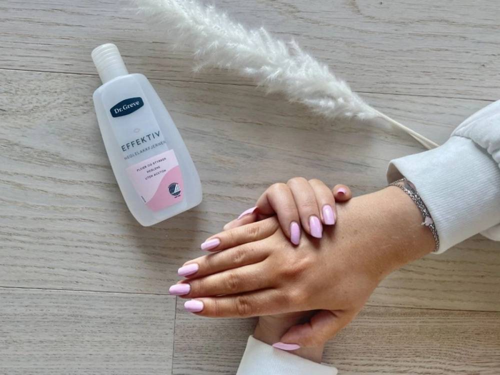 Hender med nylakkerte negler som blir tørket med hånddesinfeksjon på et lyst trebord