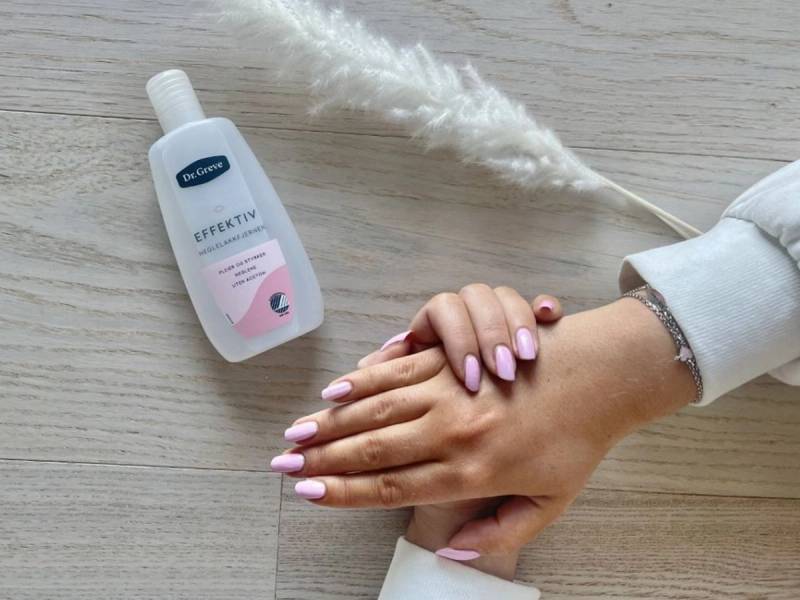 Hender med nylakkerte negler som blir tørket med hånddesinfeksjon på et lyst trebord