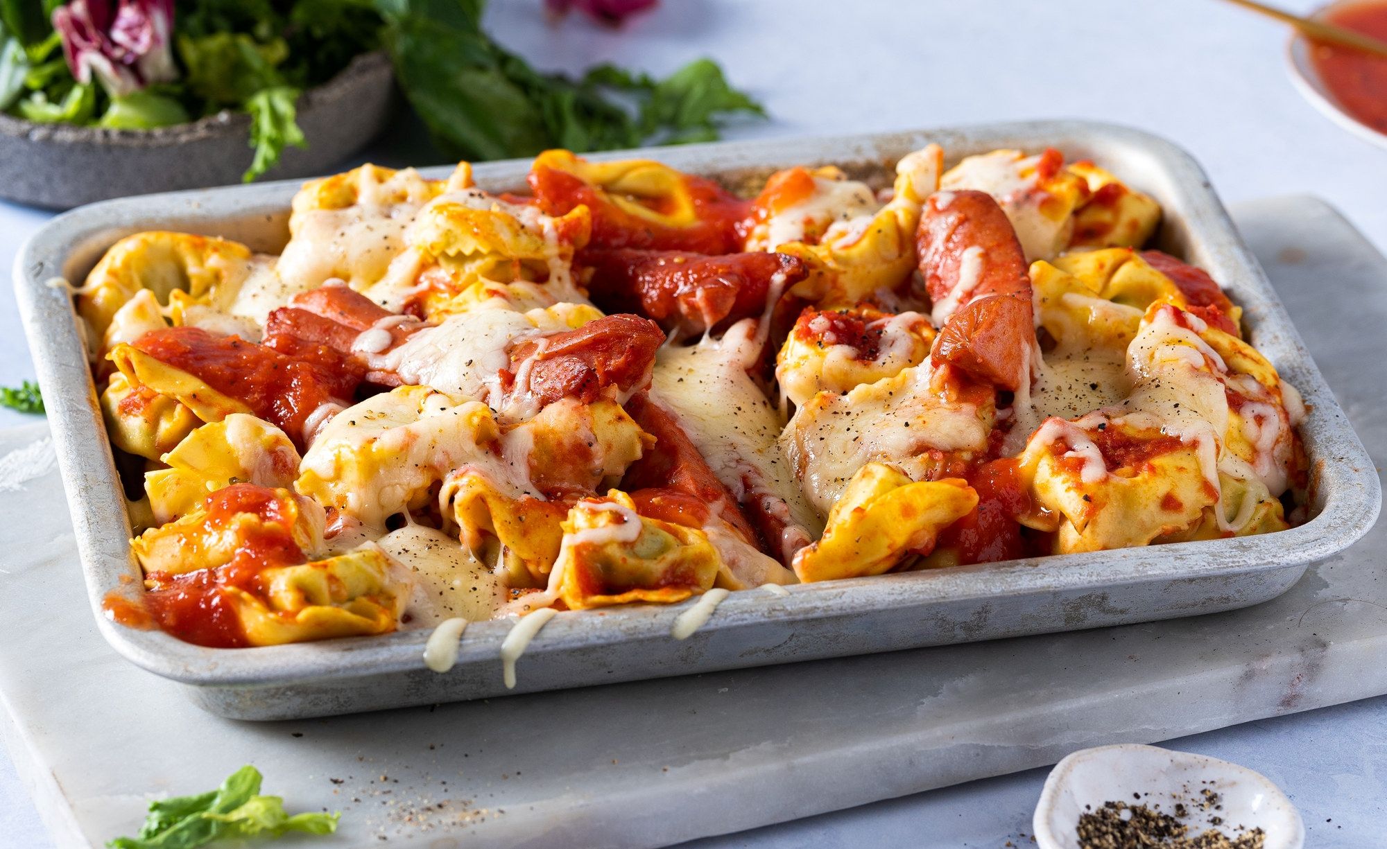 Pastagrateng med pølser, ost og tomatsaus i en ildfast form.