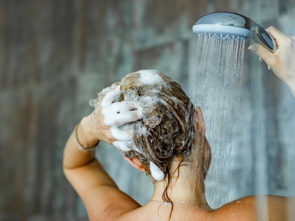 En person vasker håret under dusjen med såpe i håret.
