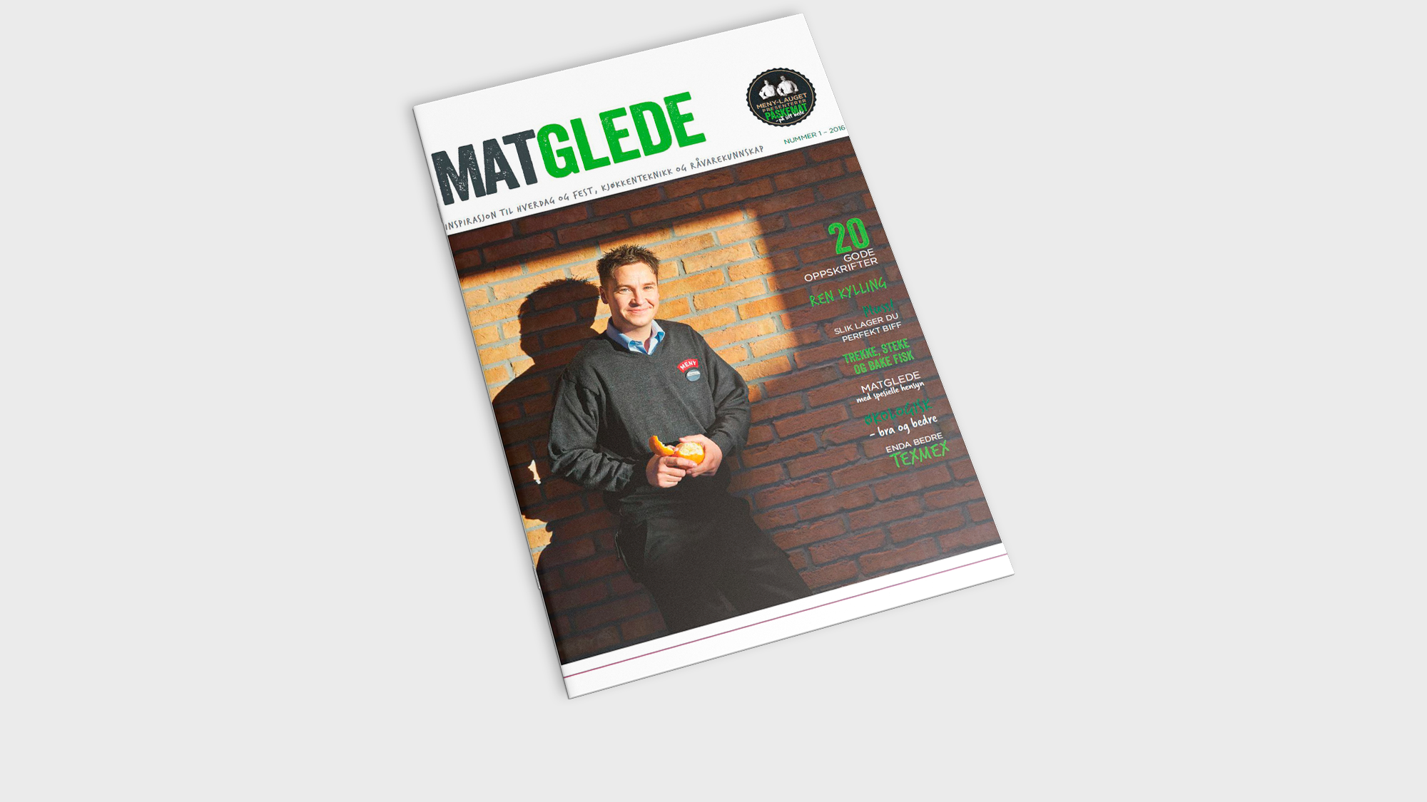 Forside av MatGlede med to personer som smiler og holder mat, mot en murvegg, med grønn og hvit tekst.