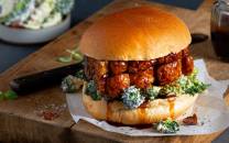 Ribbesandwich med broccolisalat på en treplate, med en liten glass med saus i bakgrunnen.