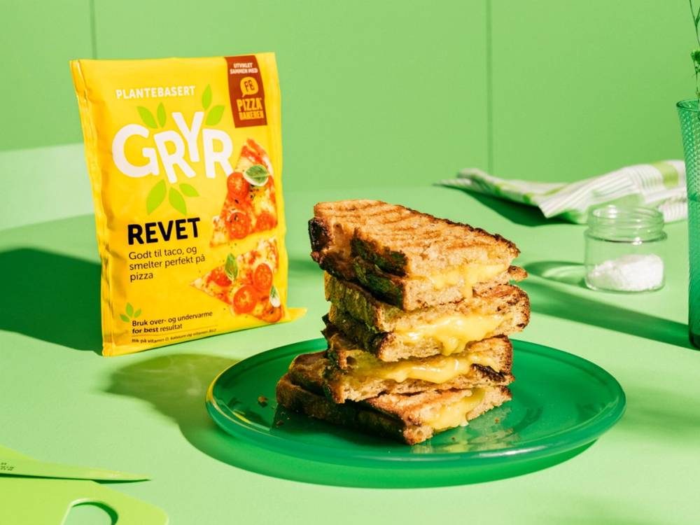 Tre lag med gryterett på en grønn tallerken, omgitt av en pakke med Gryr Revet og andre matvarer på en grønn bakgrunn.