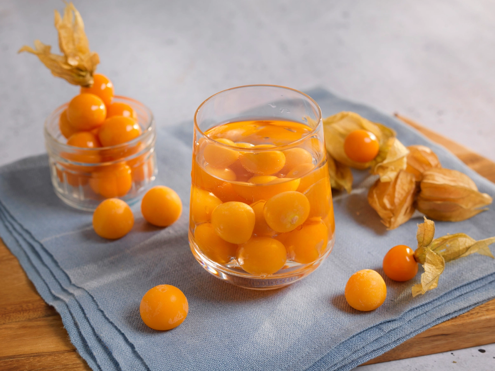 Isbiter formet som små gule bær i et glass og rundt på et blått stoff, med noen bær i en plastpose i bakgrunnen.