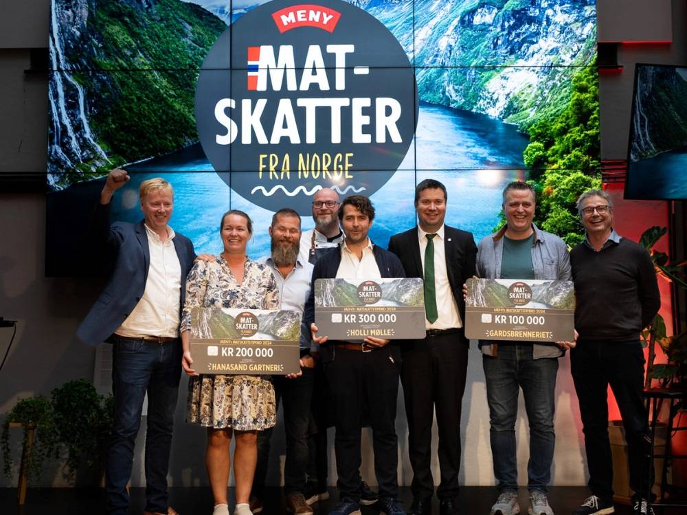 Gruppemennesker som mottar priser under en utdeling, med en stor banner som sier 'Mat-skatter fra Norge' i bakgrunnen.