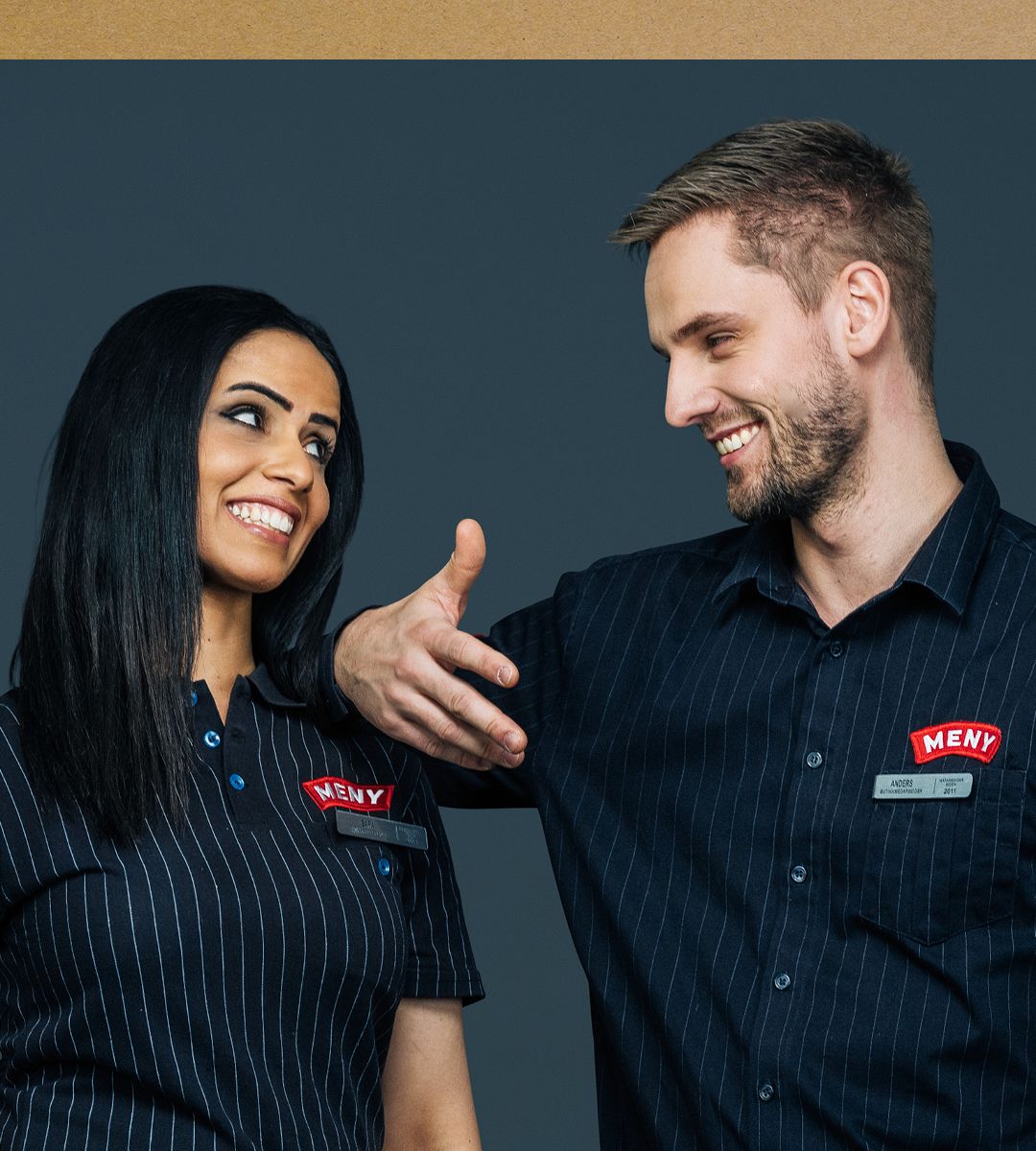 To ansatte i uniform med navnemerker står sammen og smiler, noe som kan symbolisere inkludering og mangfold på arbeidsplassen.