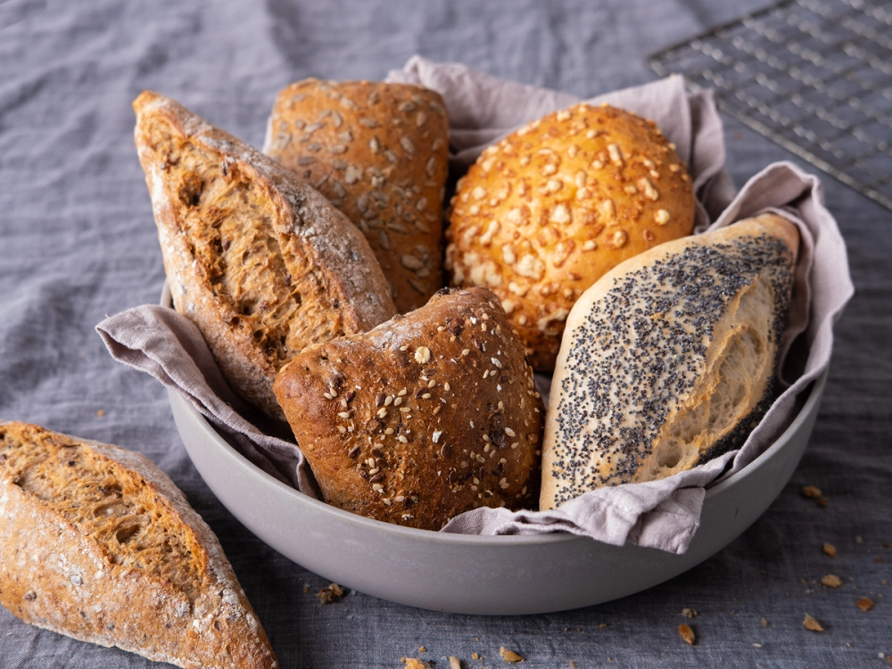 Variert utvalg av ferske rundstykker med ulike typer og toppinger i en kurv på et bord.