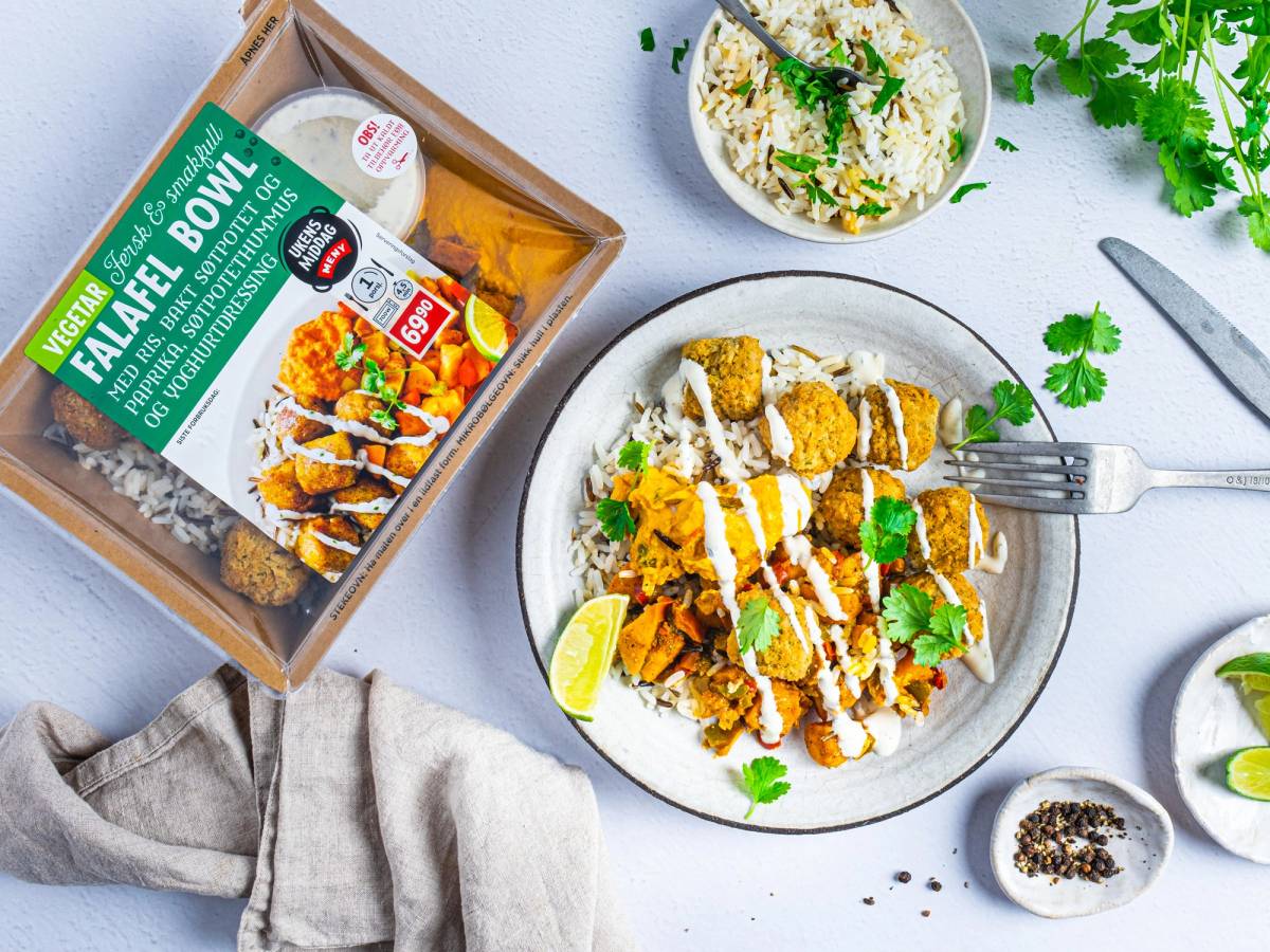 En tallerken med falafel, salat og dressing, med en pakke falafel på siden og friske urter i bakgrunnen