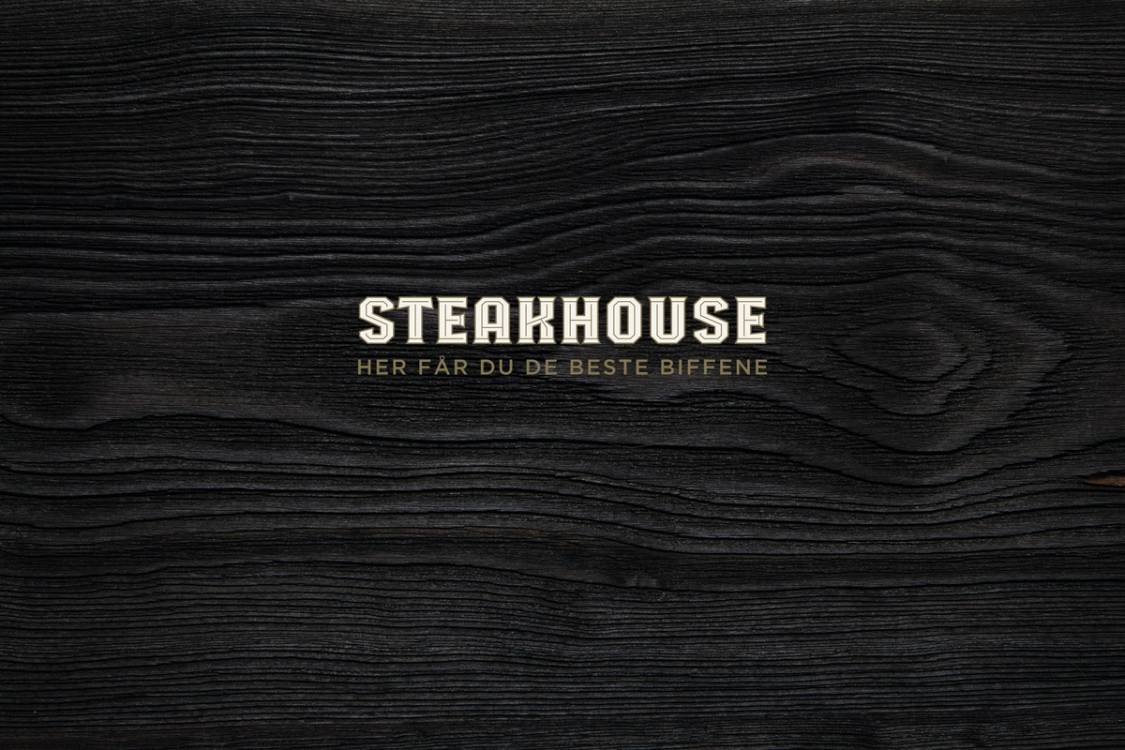 Logo for steakhouse med teksten 'Her får du de beste biffene' på en mørk trebakgrunn.