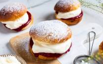 Tre fastelavnsboller med krem og syltetøy på et fat, pyntet med melis og omgitt av andre bakverk.