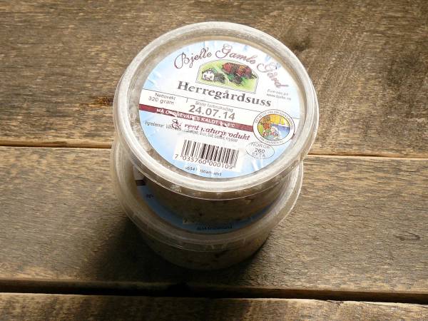 En glasskrukke med et etikett som viser Bjelle Gård, plassert på en treoverflate.