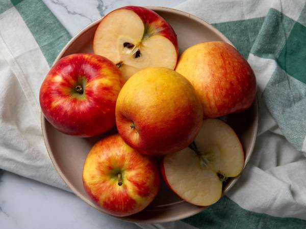 En tallerken med fire norske epler, hvorav to er skåret i biter, plassert på et bord med et grønt og hvitt rutete stoff.