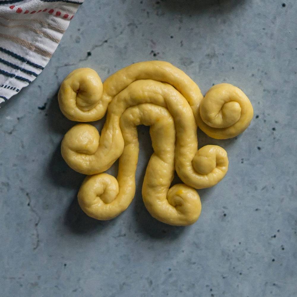 Lussekatt formet som en prest med hår av deig, plassert på en grå overflate.