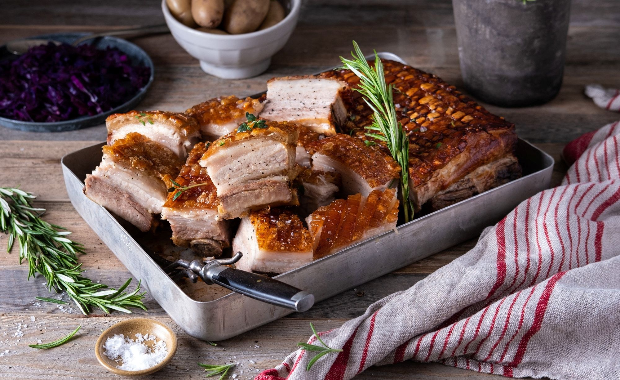 Skarer ribbe med sprø svor på et fat, omgitt av krydderurter og tilbehør.