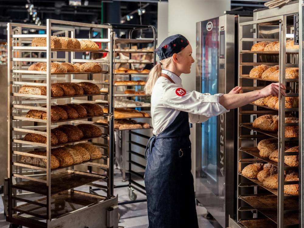 En person i bakeruniform som tar ut ferske brød fra en ovn i et bakeri.