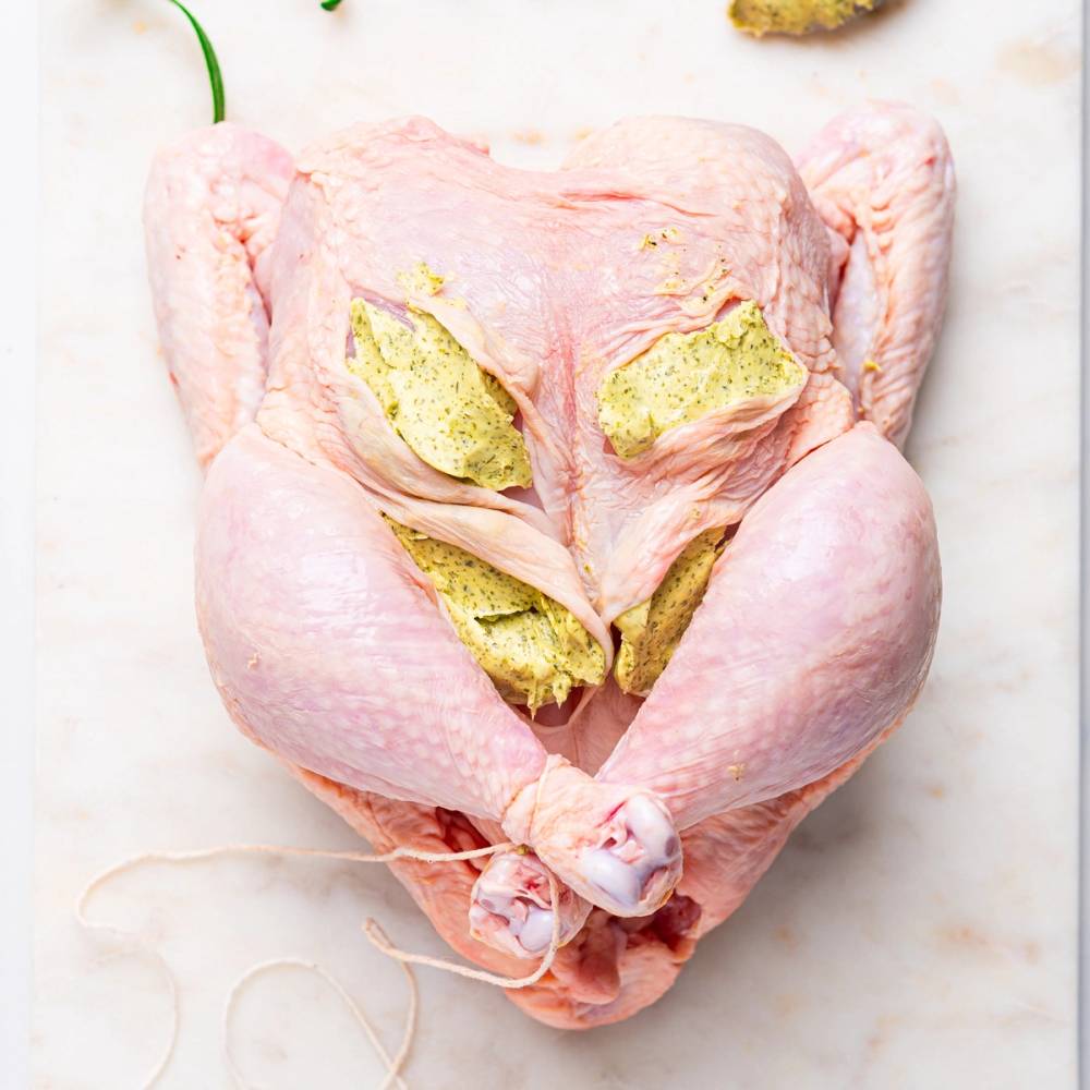 Helstekt kylling med urtesmør og ovnsbakte grønnsaker, sett på et hvitt underlag